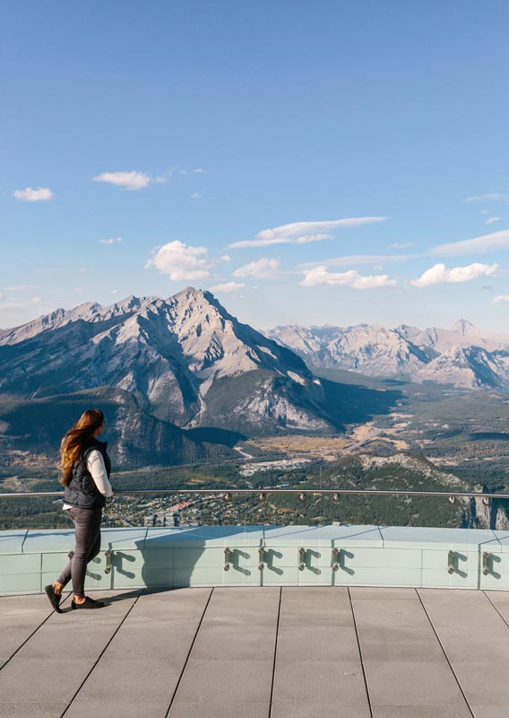 A woman looks out at mountains and forests from the top of the Banff Gondola.