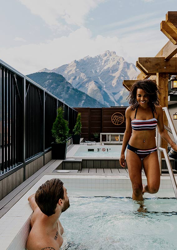 Two people at a rooftop hot tub, mountains in the distance.