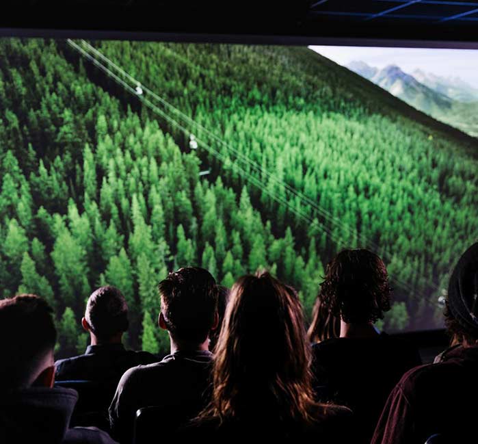 A Crowd sits and watches a film featuring the Banff Gondola cabins moving above the treeline