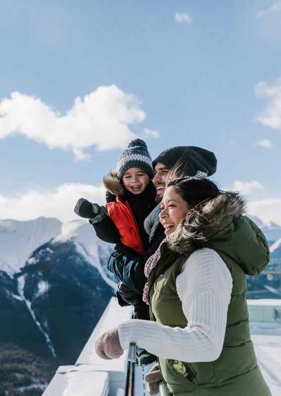 A family bundled up for the winter stands at the Banff Gondola viewpoint looks over a snowy valley