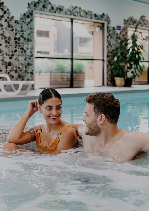 A man and woman sit in an indoor hot tub