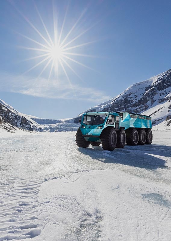 An Ice Odyssey vehicle drives on a glacier between two mountains.