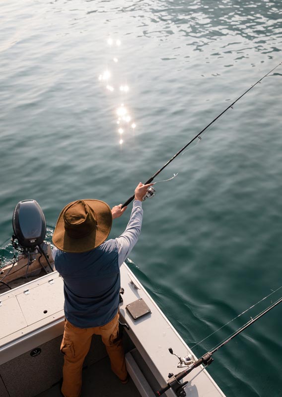 An angler casts a fishing rod into a lake off the back of a motor boat.