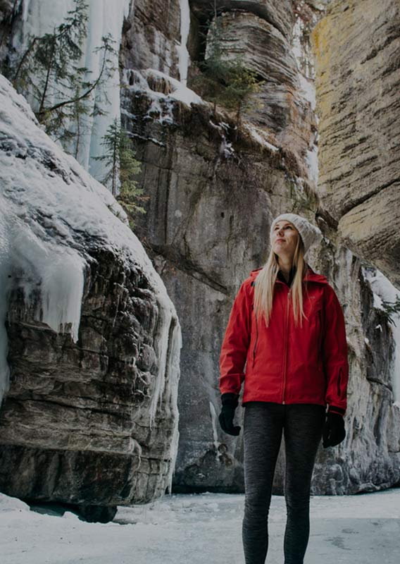 A woman in a red jacket stands in an icy canyon