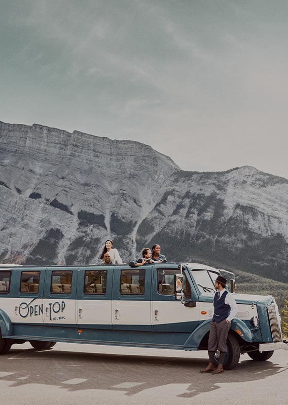 A historic style bus stopped at the side of a road. A tall mountain behind.