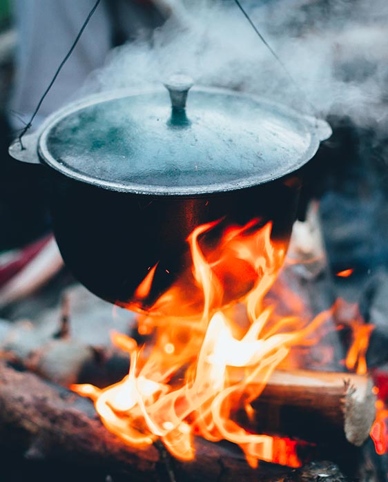 A cast iron pot hanging over a roaring bonfire.