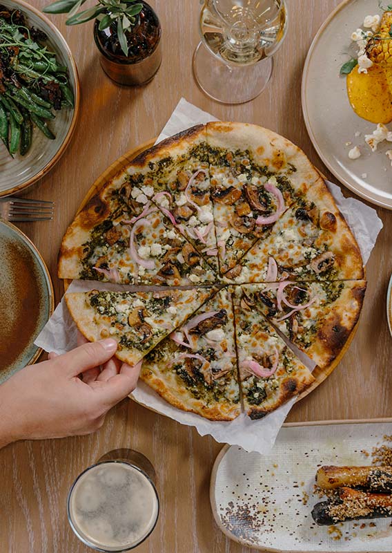 A pizza and side dishes on a wooden dining table.