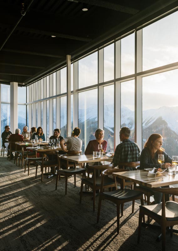 A dining room with floor-to-ceiling windows looks out onto snow-capped mountains.