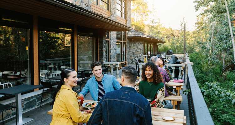 A group of friends sit at an outdoor patio table enjoying food and beverages.