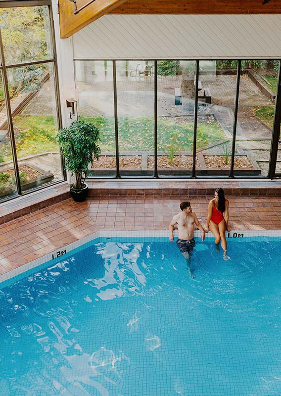 An indoor swimming pool with two people sitting at the edge.