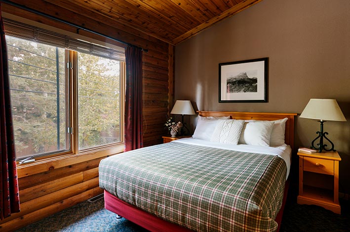 A bed in a wooden cabin next to a large window looking out to trees