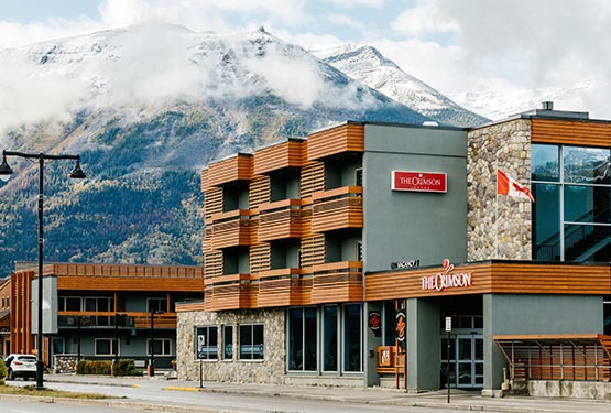The Crimson hotel along a road against a backdrop of snow-dusted mountains.