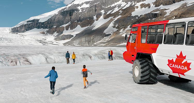 People walk on the glacier, a large tour bus behind.
