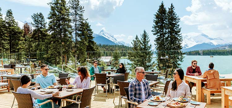 People sitting on a dining patio with mountains and a lake in the background