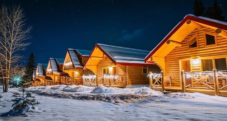 A row of wooden cabins covered in snow and lit up at night..