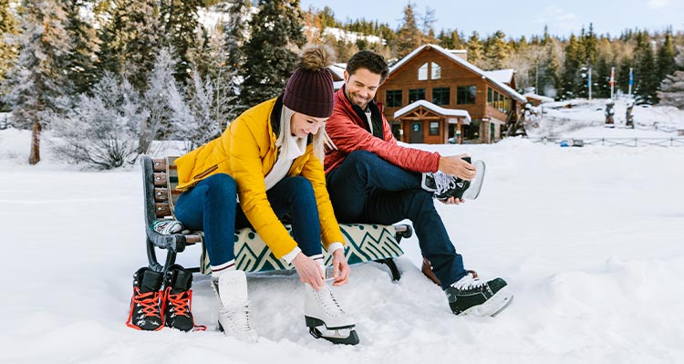 Two people sit on a bench, putting on ice skates.