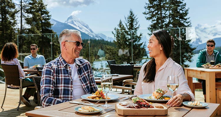Two people sit at a dinner table on a patio by a lake.