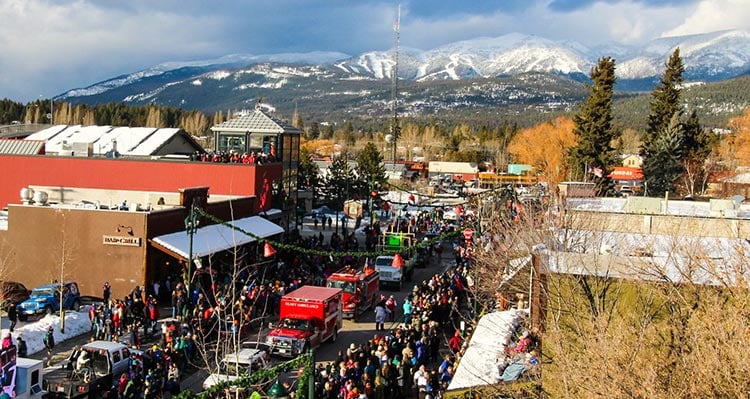 A parade goes down a busy street in Whitefish, Montana. Snowy mountains in the distance.