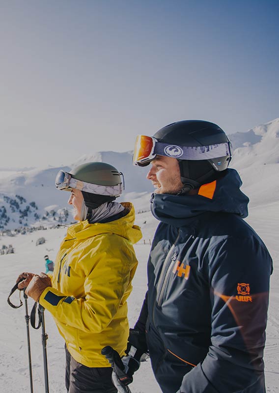 A couple in ski gear looks down a snowy hill