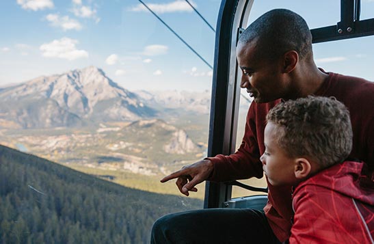 A man and child look out the Banff Gondola, overlooking a wide valley.