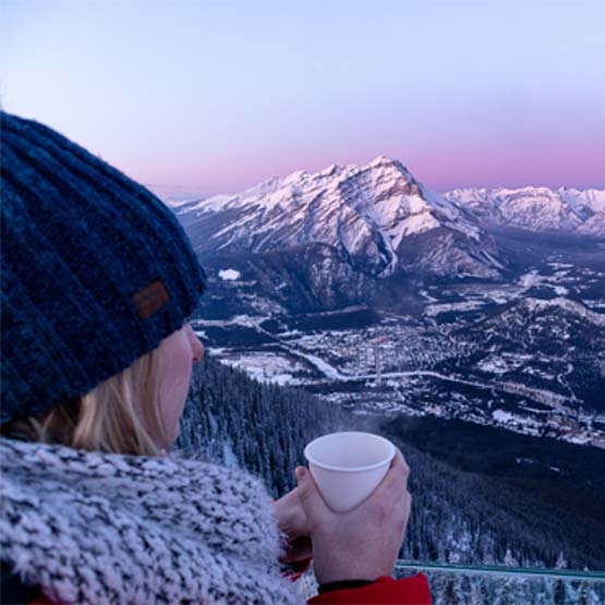 Visitor holding a beverage, looking at the mountains