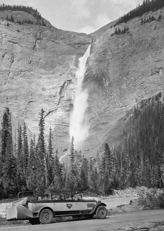 A historic style bus with waterfall in the background.