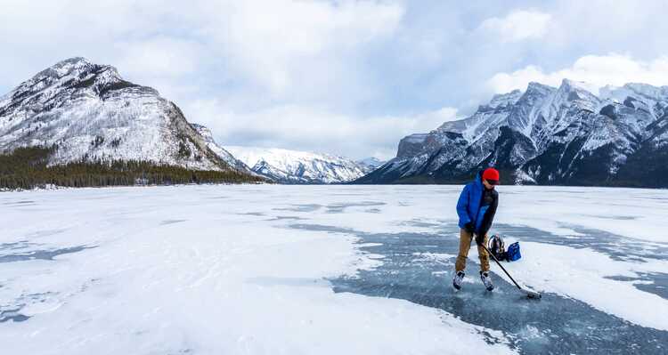 An ice skater on a frozen lake between mountains.