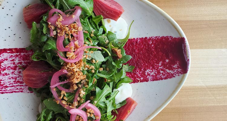 A salad of greens topped with pickled onions and crumbled nuts.
