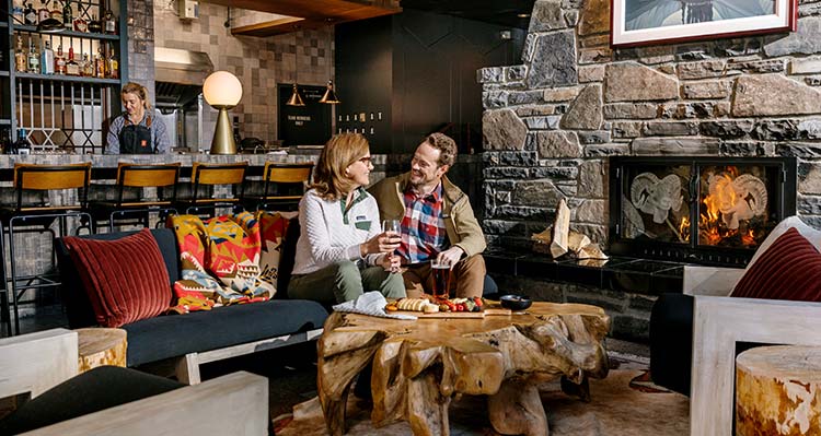 A couple sits at Maligne Canyon Wilderness Kitchen near a fireplace.