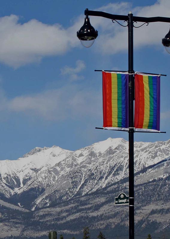 A view of snow-covered mountains behind pride flags hanging on a lamp post.