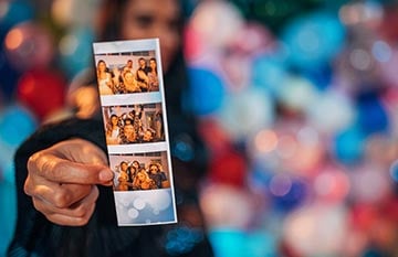 A person holds up a set of printed photo booth pictures.