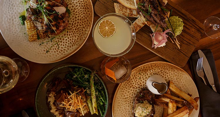 An overhead view of a dinner table, with plates of food and drinks,