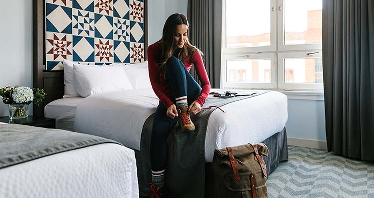 Lady putting on her hiking boots while sitting on hotel bed