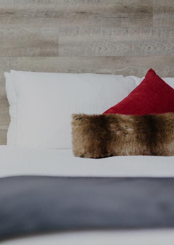 A hotel bed with red and brown pillows