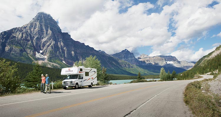 Two people walking along road with RV parked by a lake