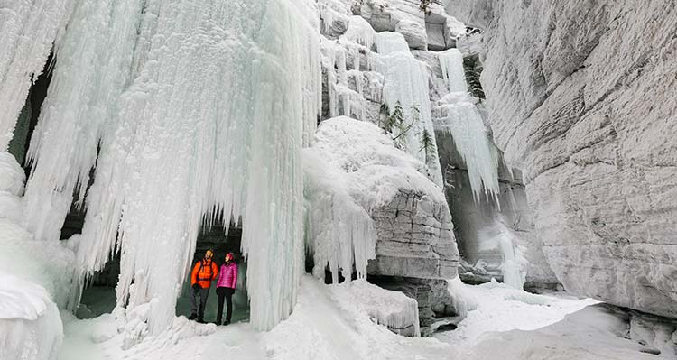 A couple stands under a frozen waterfall within the Maligne Canyon.