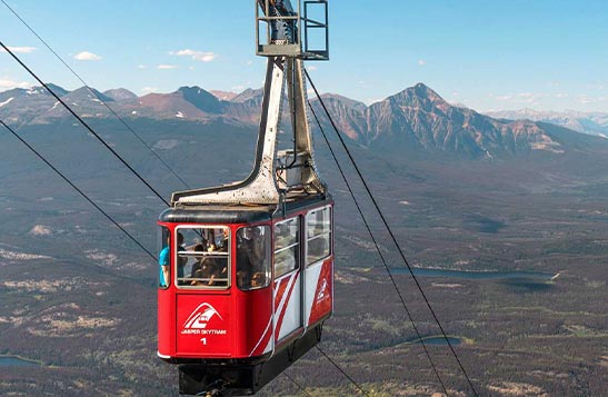 A red aerial tramway ascends up its cable high above a forested valley.