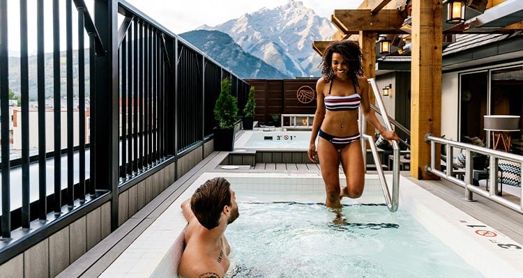 Two people enter a hot tub on a rooftop patio.