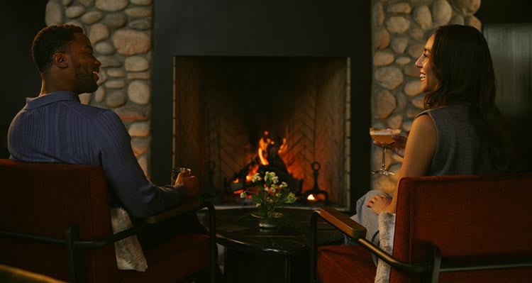 Two people sit at a fireplace